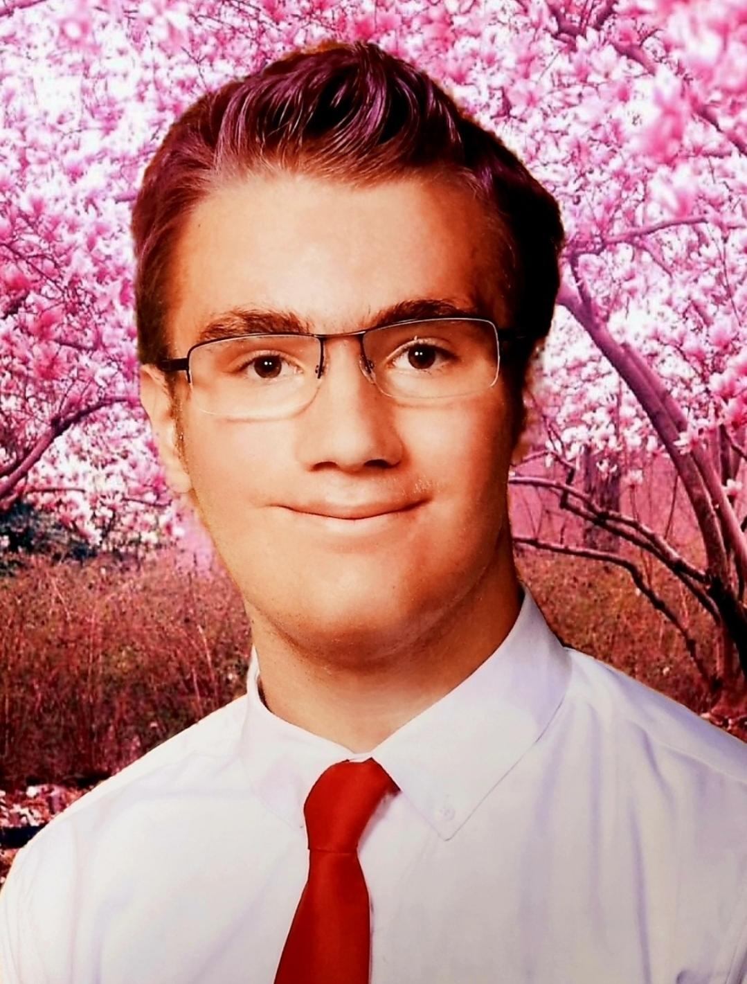 Rio, the creator of this page, wearing a white button up shirt with a red tie. Cherry blossom trees are in the background.